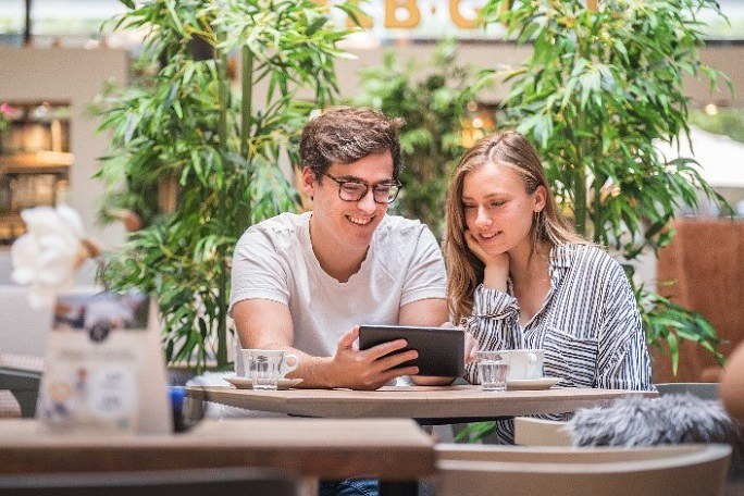 Zwei Jugendliche sitzen in einem Café und schauen gemeinsam auf ein Tablet.