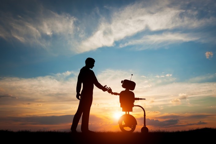 Ein Mann und ein Roboter, die sich im Sonnenuntergang die Hand geben.