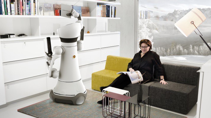 Eine Frau liest eine Zeitschrift auf einem Sofa. Ein Roboter holt ein Buch aus dem Schrank. 