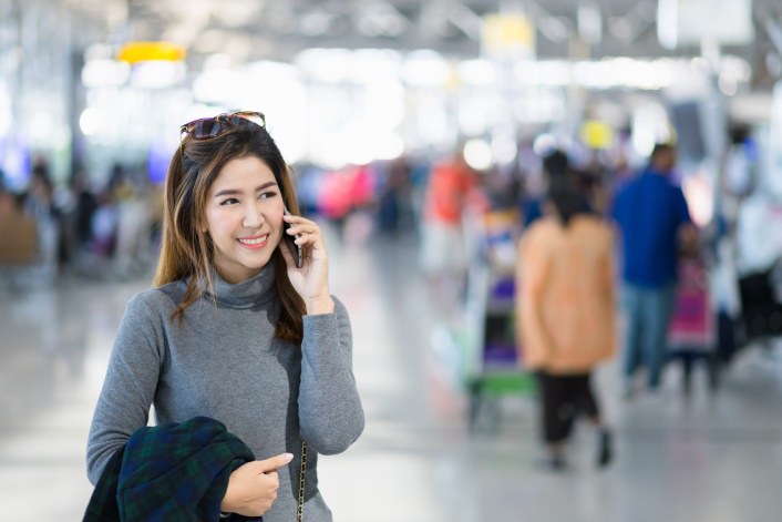 Eine Frau hält ein Smartphone am Ohr. Sie befindet sich an einem Flughafen.