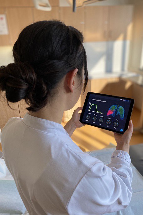Eine Frau im Arztkittel schaut auf ein Tablet mit der grafischen Darstellung einer Lunge und diversen Diagrammen.