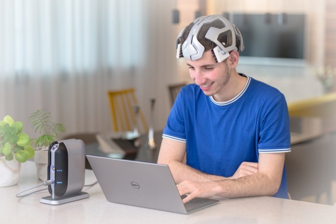 Mann mit CogniTor-Elektrostimulations-Helm sitz vor einem Laptop