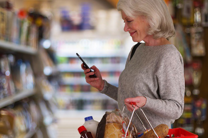 Ältere Frau im Supermarkt mit Smartphone in der Hand