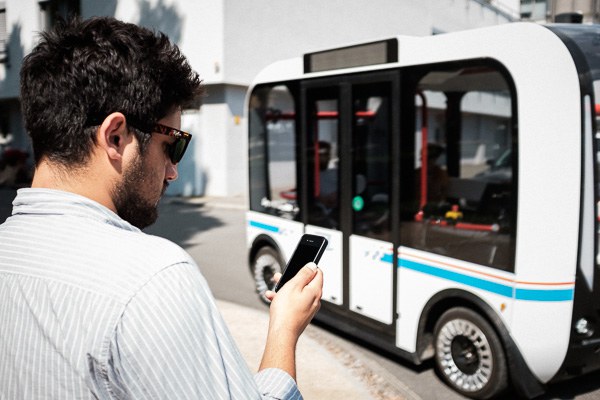 Ein Mann mit einem Handy in der Hand, ein Bus im Hintergrund. 