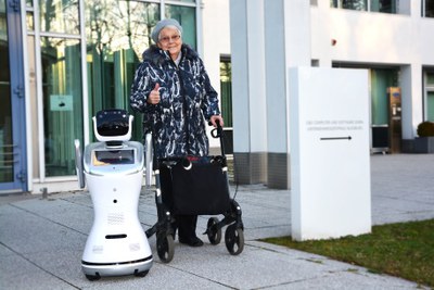 Alte Frau mit Rollator neben Roboter aus Straße