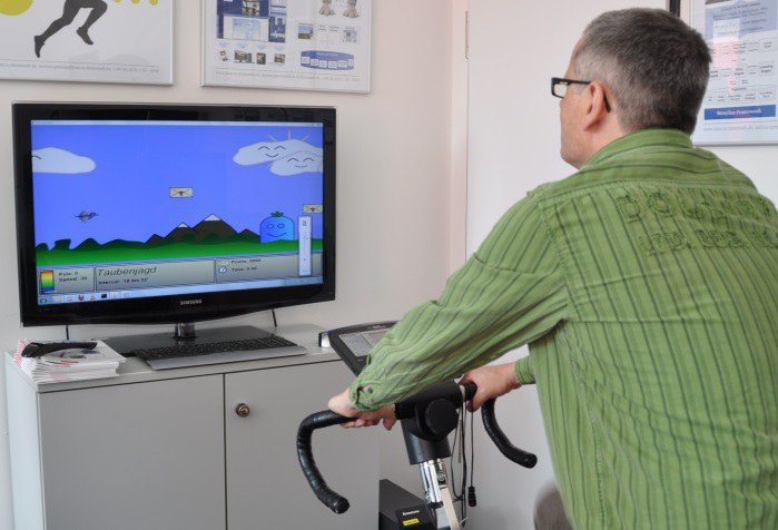 Ein Mann auf einenm Fahrrad Ergometer, der auf einen Bildschim schaut. 