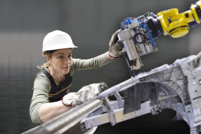 Eine Frau an einem Metallgerüst und ein Roboterarm. 
