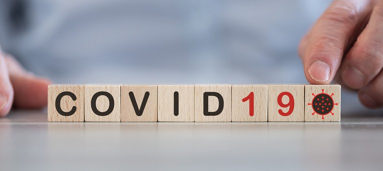 Nachaufnahme von Bauklötzen mit den Buchstaben COVID19 und einem Virus-Symbol, die nebeneinander auf einer Oberfläche liegen